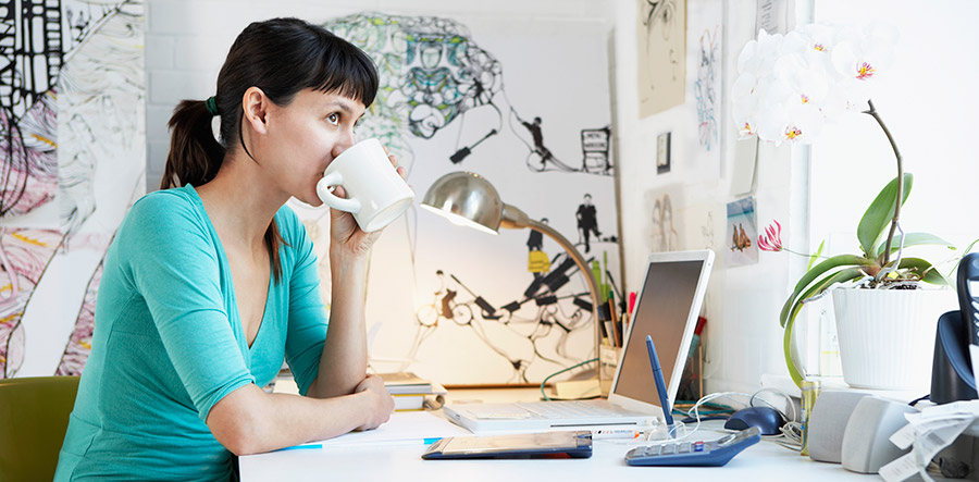 Woman drinking coffee at in front of laptop